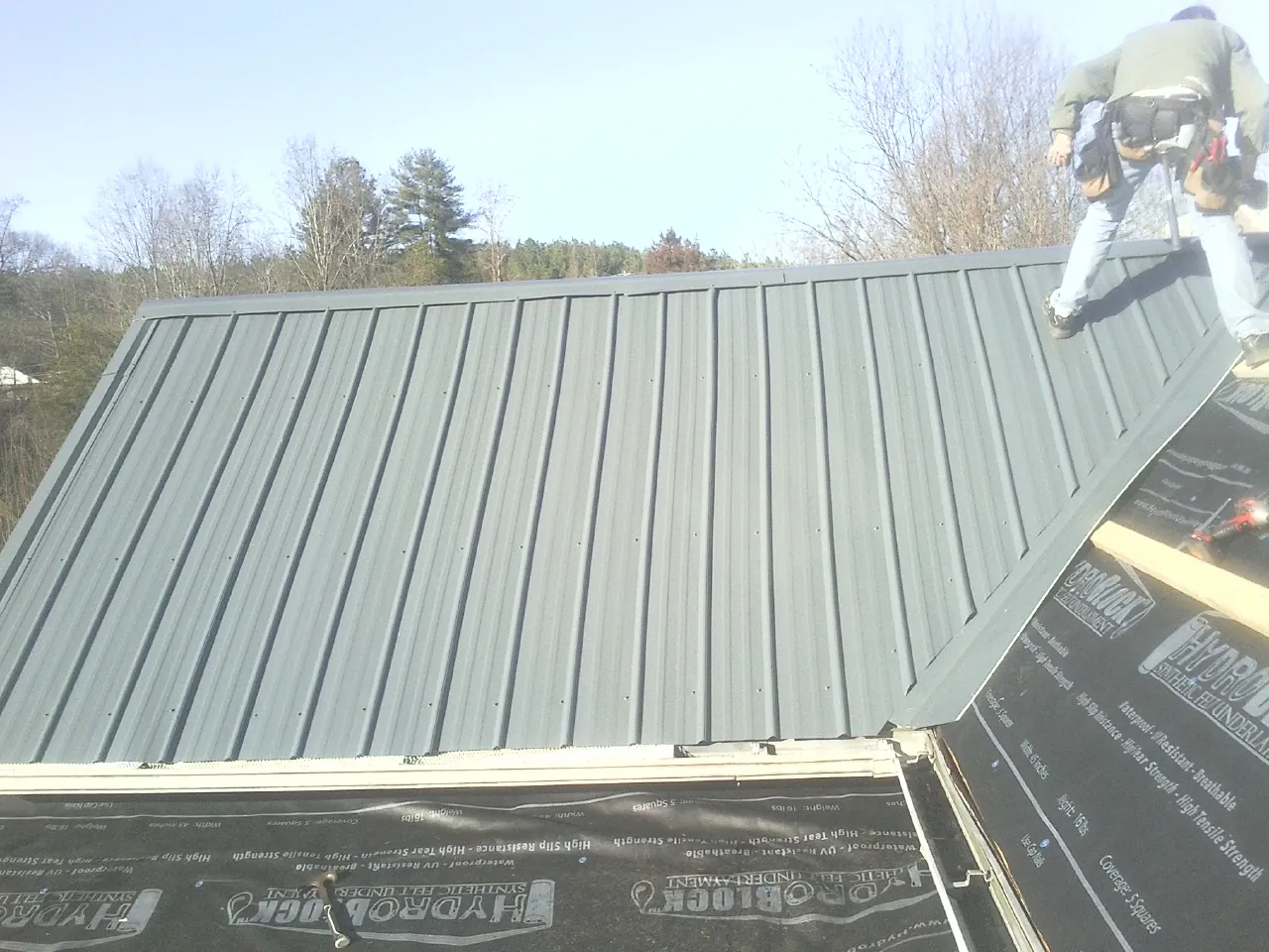 Crew installing dark green standing seam panels over synthetic underlayment in East Elmhurst