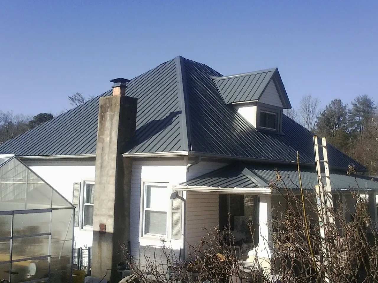 Dark blue standing seam metal roof on a white farmhouse with dormer — Slate & Tile Roof Repair by Roofing Brothers in East Elmhurst
