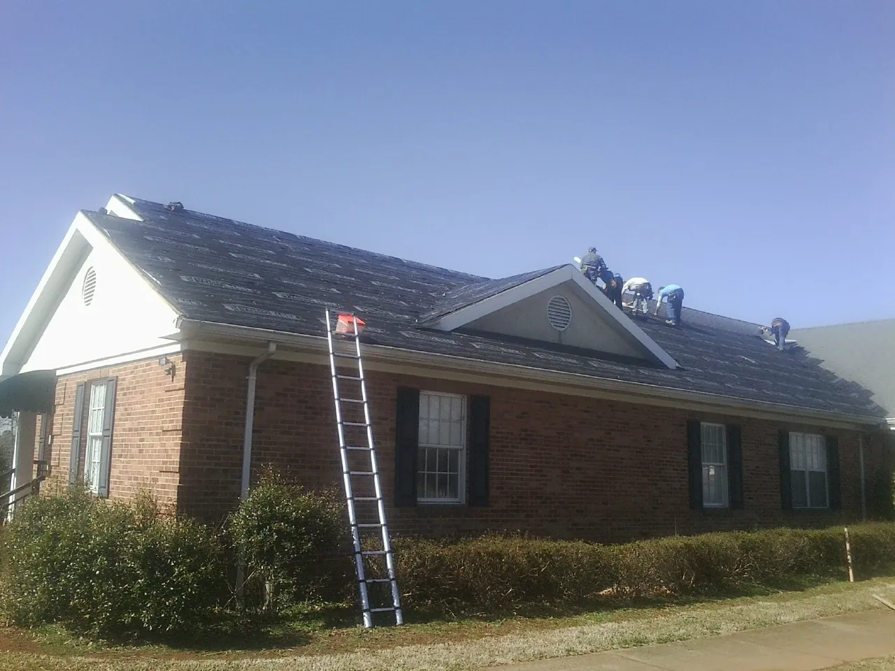 Crew tearing shingles off a brick ranch roof with a ladder set — Emergency Roof Repair work by our crew in East Elmhurst