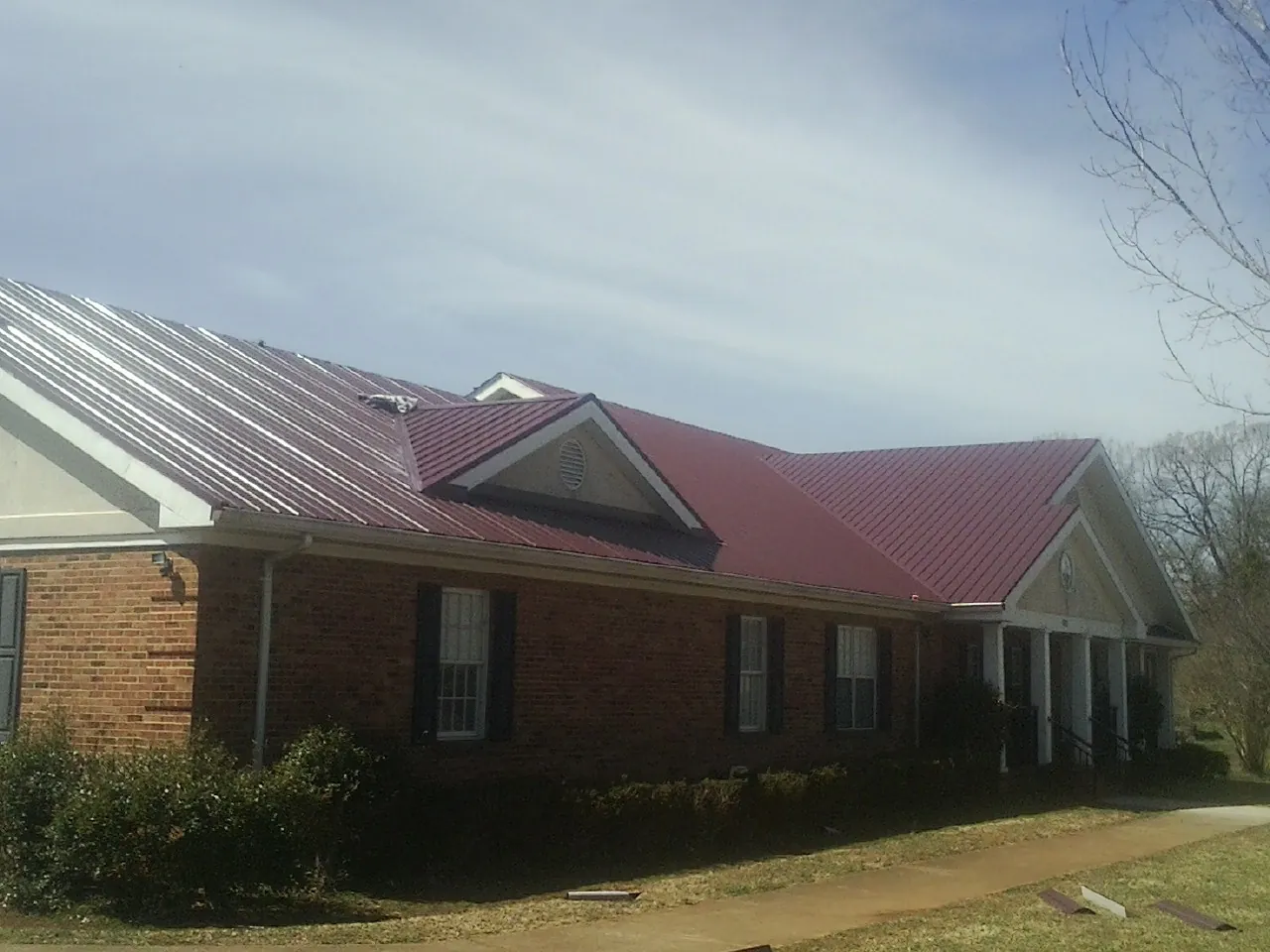 Red metal roof with gabled entries on a long brick building, from a Hail Damage Roof Repair job in East Elmhurst