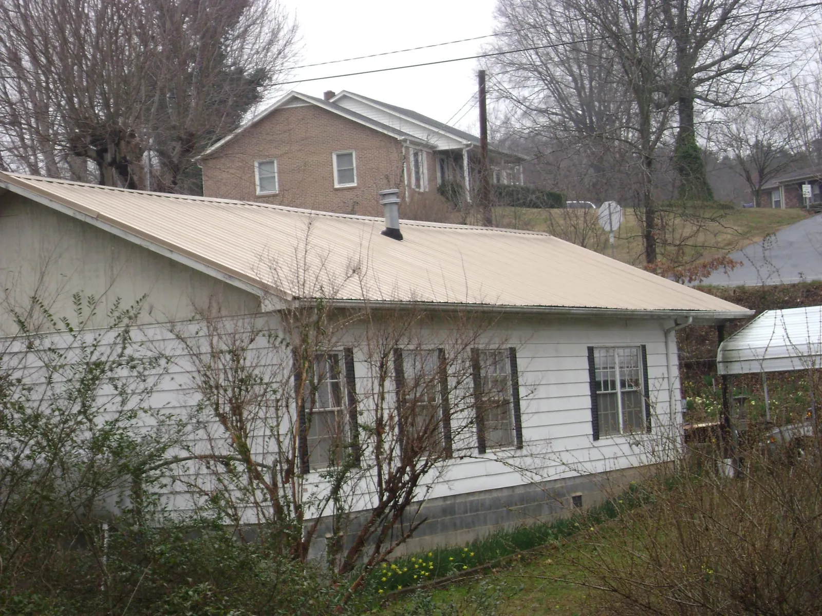 Tan metal roof on a white sided house set into a hillside — Commercial Roofing by Roofing Brothers in East Elmhurst