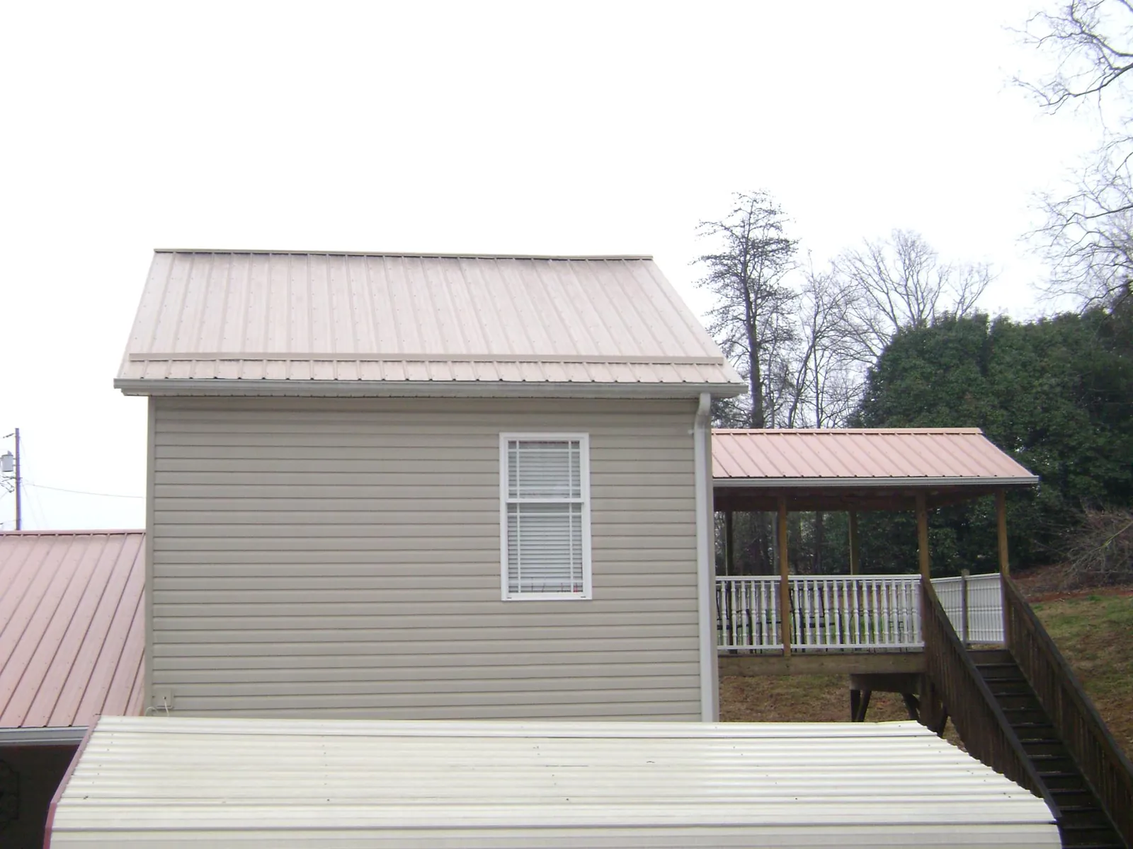 Tan metal roofs on a two story addition and attached porch, from a Roof Replacement job in East Elmhurst